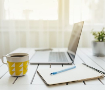 laptop next to coffee mug and notepad
